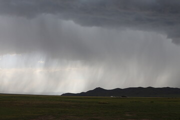 Regen fällt aus dichten Wolken auf die Berge am Horizont der mongolischen Steppe und verdeutlicht die ungezähmte Natur der Landschaft.