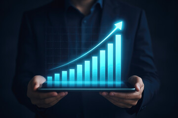 Hands holding tablet showing glowing blue bar chart and upward trending arrow over dark background finance