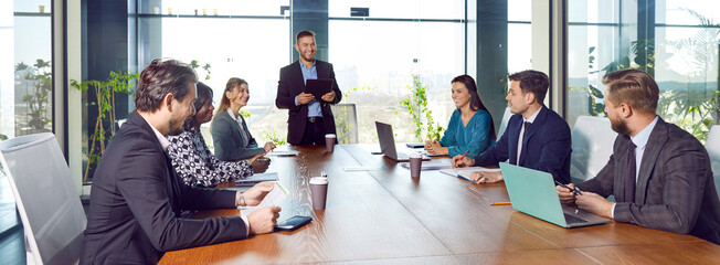 Diverse joyful confident people sitting at big table in meeting room having business conference in modern office. Company employees discussing new projects at working place. Teamwork concept. Banner.