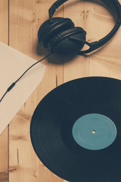 Close-up of headphones on a wooden table next to a vintage vinyl record