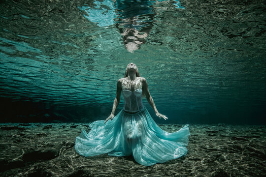 Mid adult woman with tattoos in a strapless gown sitting underwater on the seabed