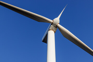 Close-up view of a modern wind turbine against clear blue sky. Renewable energy technology and sustainable electricity production concept.
