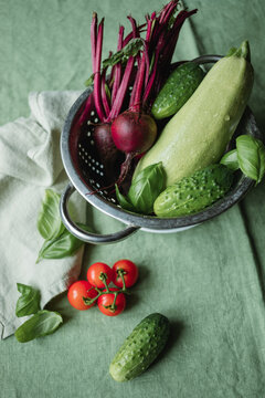 Close-up overhead view of beetroot, courgette, cherry tomatoes and cucumbers in a metal colander on a green tablecloth