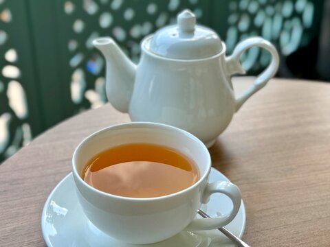 Close-up of a cup of green tea on an outdoor table with a teapot