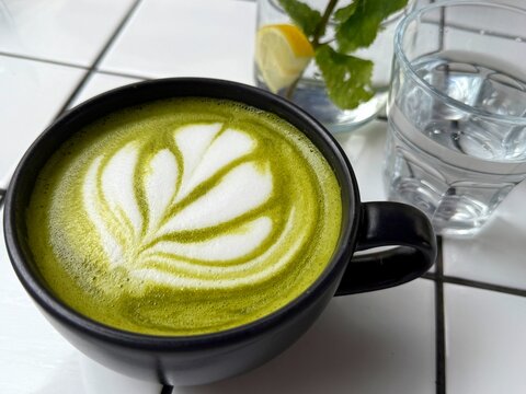 Close-up of a matcha latte with a glass of lemon and mint water on a table