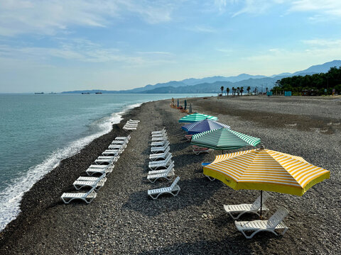 Rows of plastic Sun loungers and parasols on an empty pebble beach in summer, Batumi, Adjara, Georgia