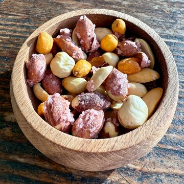 Close-up of a bowl of assorted salted peanuts, toasted corn and hazelnuts on a wooden table