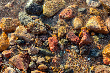 Colorful wet pebbles and natural stones on sandy beach shore with sea water waves, close up textured background, summer vacation nature scene, relaxation, tranquility, travel, coastal environment conc