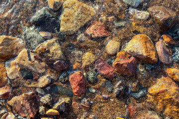 Colorful wet pebbles and natural stones on sandy beach shore with sea water waves, close up textured background, summer vacation nature scene, relaxation, tranquility, travel, coastal environment conc