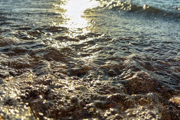 Golden sunset light reflecting on sea waves washing over  and pebbles on the beach shore, relaxing ocean water texture background, natural coastal landscape scene for travel and nature themes.