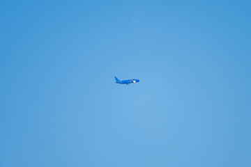 A solitary blue airplane glides through a pristine, cloudless sky at cruising altitude.