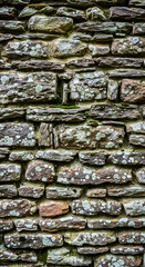 Closeup of an old stone wall with moss and lichen growing on the surface, showcasing the texture and age of the stones, creating a rustic and weathered appearance in a vertical composition
