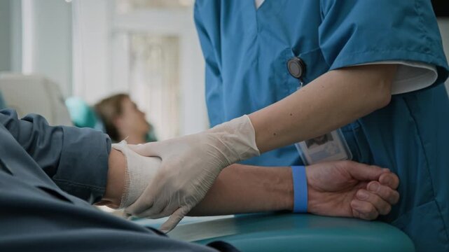 Close-up shot of unrecognizable nurse, wearing gloves and scrubs, applying bandage to arm of man after donating blood in clinic
