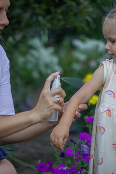 Mother applying insect repellent spray on childs arm outdoors. Selective focus