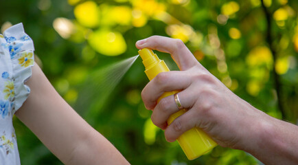 Father applying insect repellent spray to child's hand outdoors. Selective focus © Anna