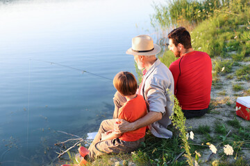 Grandfather, father and his little son fishing together near river outdoors