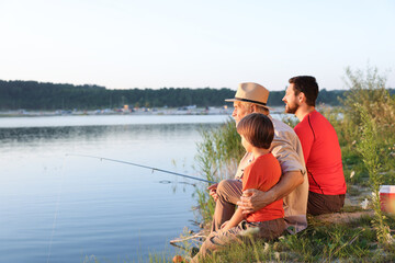 Smiling grandfather, father and his little son fishing together near river outdoors