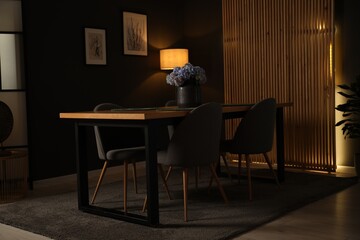 Wooden table with beautiful flowers and chairs in dining room at night