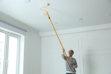 Young woman painting ceiling with white dye indoors, space for text