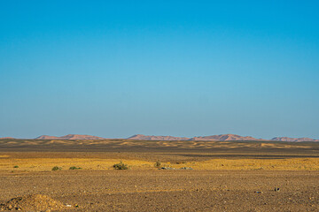 Flat Sahara desert plain in Morocco with dry rocky ground distant low hills and clear blue sky stretching across wide barren arid landscape view