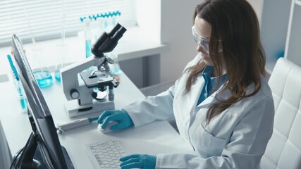 A dedicated female scientist in a lab coat analyzes data with a microscope and computer, surrounded by equipment and vibrant test tubes, showcasing her commitment to scientific discovery