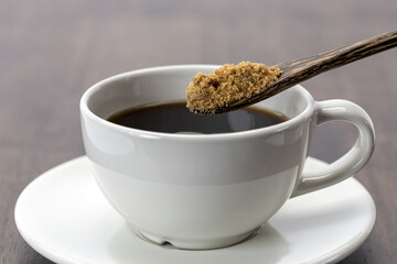 Black coffee with full brown sugar spoon, white ceramic cup and saucer on wooden table, morning beverage, warm and inviting atmosphere