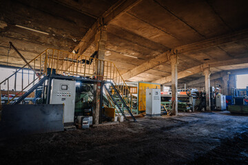 Interior of an industrial woodworking factory with heavy machinery, control panels, and metal stairs in a large concrete building with natural light.