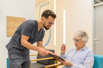 Male doctor in eyeglasses giving medical documents to elderly woman for signature during hospital visit