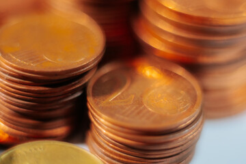 Close-up macro image of a shiny 2 euro cent coin on top of a stack, highlighting its texture and detail under warm lighting with a soft background blur.