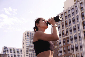 Sporty girl in sportswear holding bottle of water during break after jogging to refresh herself, exercise outdoors. Healthy lifestyle concept
