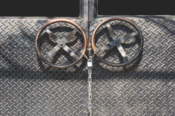 Black metal door made from carbon steel diamond plate with circle door handle and padlock in industrial vintage loft style, front view with copy space