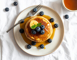 Banana Pancakes with Blueberries and Maple Syrup on Ceramic Plate