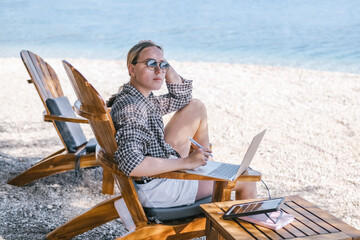 Beach workation digital nomad plans tasks with laptop and notebook on lounge chairs, powered by a...
