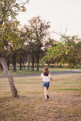 Child explores a sunlit park, feeling the warmth of an early evening breeze while surrounded by gentle trees and soft grass