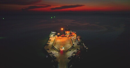 Aerial drone of a ferry docking in Moo Koh Ang Thong National Marine Park, Thailand, at night, with cars driving off the boat and a dramatic sunset in the background