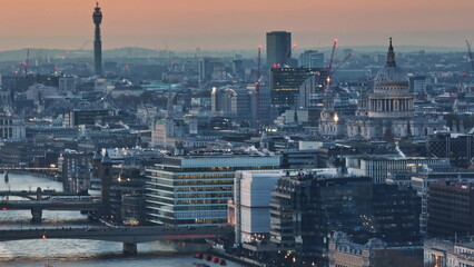 United Kingdom, London: Aerial view capturing London's iconic skyline at sunset, featuring BT Tower, St. Paul's Cathedral, and illuminated buildings along the River Thames. Drone flight