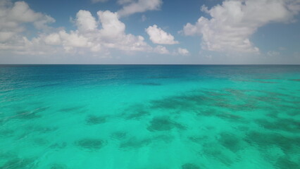 Obraz premium Breathtaking aerial view of transparent turquoise water gently merging with deep blue ocean under a partially cloudy sky, creating a mesmerizing seascape. Travel background, idyllic exotic paradise