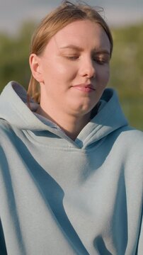 Young lady engaging in fitness exercise while kneeling forward, hair tied back, with blurred background featuring tree and unclear figures in the distance