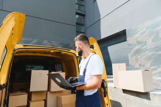 Deliveryman using laptop next to van full of cardboard boxes