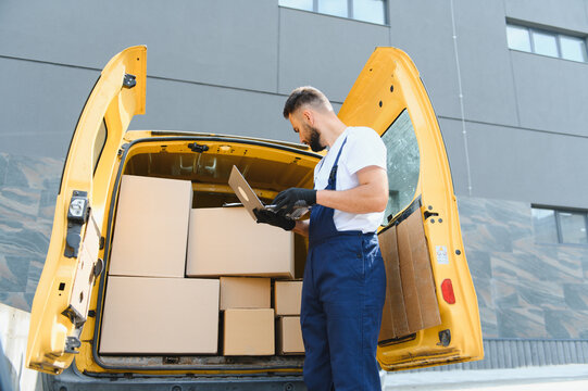 Courier checking cardboard boxes using laptop in delivery van