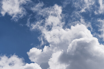Airplane flying between clouds in blue sky - travel and aviation background