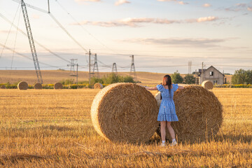 Portrait of a young beautiful dark-haired girl in a summer dress in a village field among bales of...