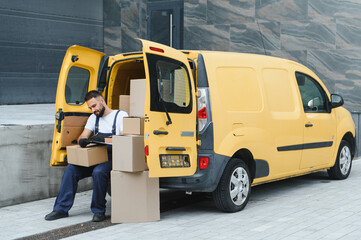 Deliveryman checking packages sitting near yellow van