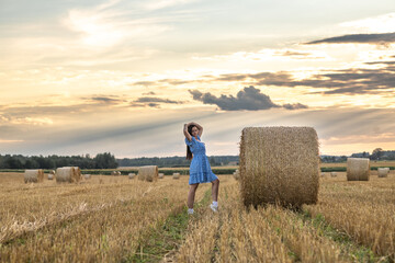 Portrait of a young beautiful dark-haired girl in a summer dress in a village field among bales of...