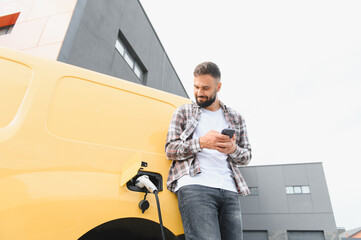 Delivery driver using smartphone while charging electric van