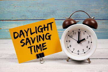 Daylight Saving Time text written on paper card with alarm clock on wooden background