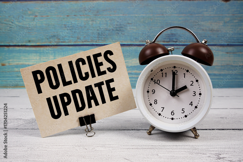 Poster policies update text written on paper card with alarm clock on wooden background