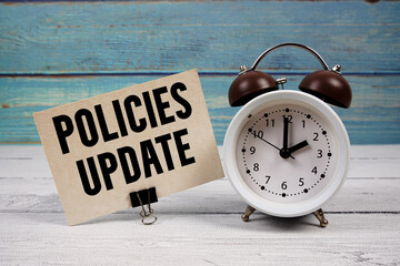 Policies update text written on paper card with alarm clock on wooden background