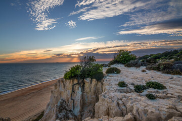 Scenic sunset over cliffs, pine forest, and golden beach in Mazagon, Huelva, Spain. Tranquil seascape ideal for travel, nature, and landscape concepts.