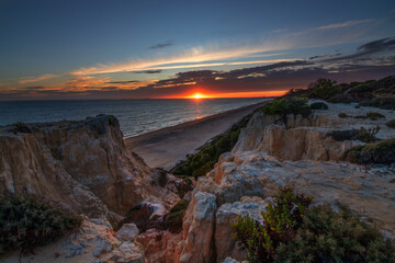 Scenic sunset over cliffs, pine forest, and golden beach in Mazagon, Huelva, Spain. Tranquil seascape ideal for travel, nature, and landscape concepts.